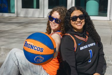 2 students in basketball jersyes with a orange and blue basketball in hand.